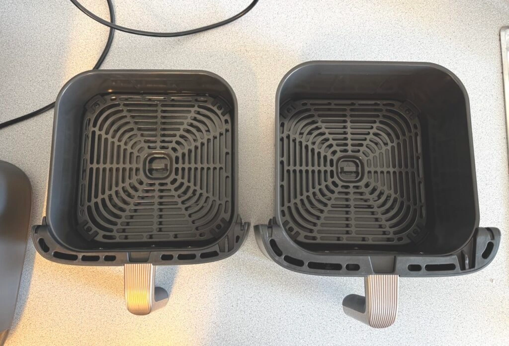 Zwei herausgenommene Frittierkörbe nebeneinander mit identischem Gitterdesign und bronzefarbenen Griffen.