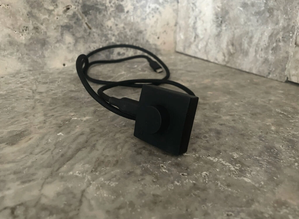 Schwarzes USB-Ladekabel des UltraHuman Ring AIR mit quadratischer Ladevorrichtung.