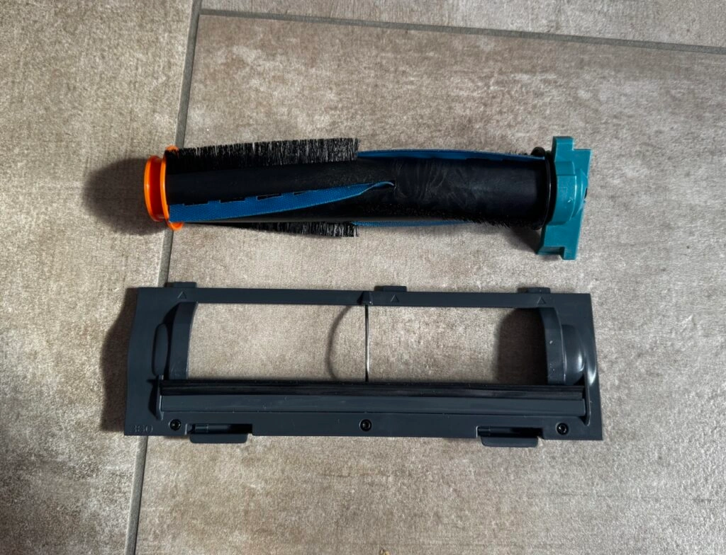 Herausgenommene Hauptbürste mit orange-blauen Borsten neben der zugehörigen Halterung.