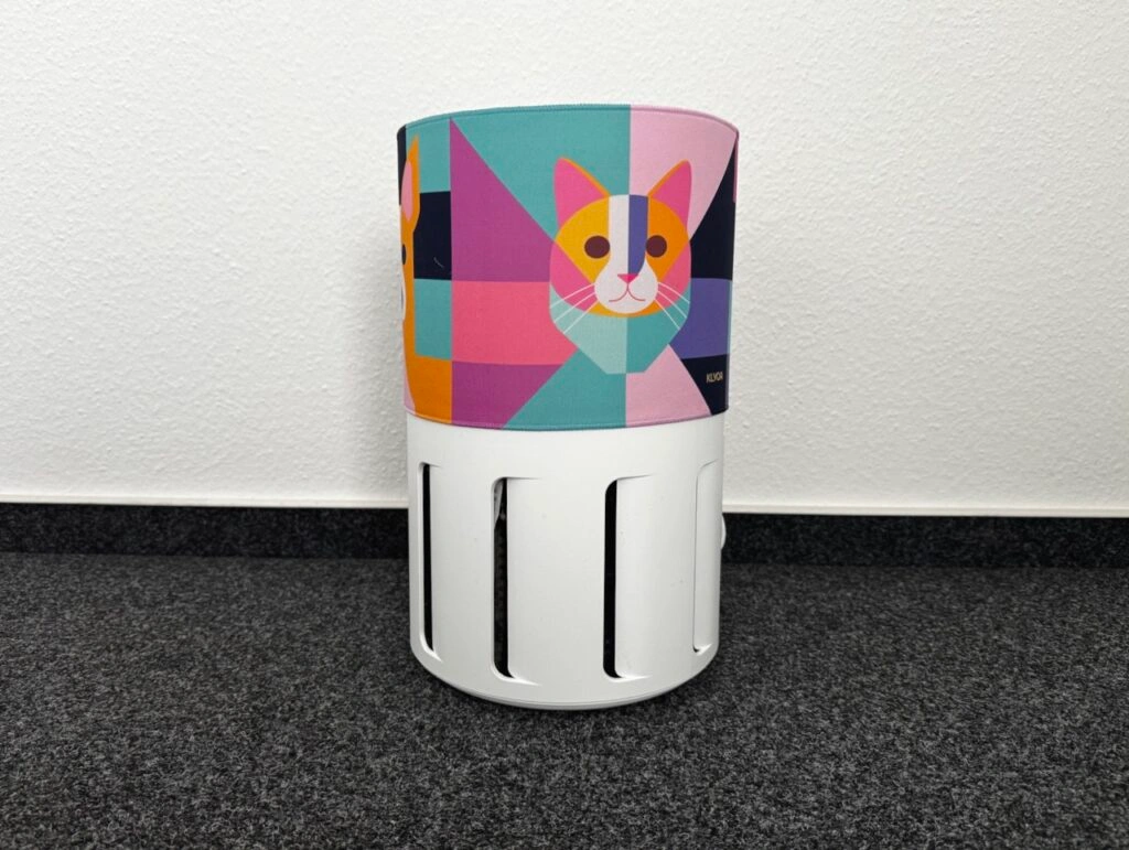 Der Luftreiniger ist mit einem bunten Überzug mit geometrisch gestaltetem Katzenmotiv versehen. Die Lüftungsschlitze unten bleiben frei.