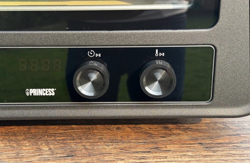 Zwei silberne Drehregler unter einem kleinen Display zeigen die einfache Steuerung von Zeit und Temperatur.
