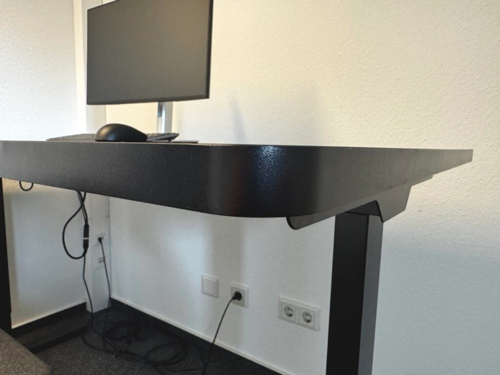 Nahaufnahme der schwarzen Tischplatte mit strukturierter Oberfläche und montiertem Monitor.
