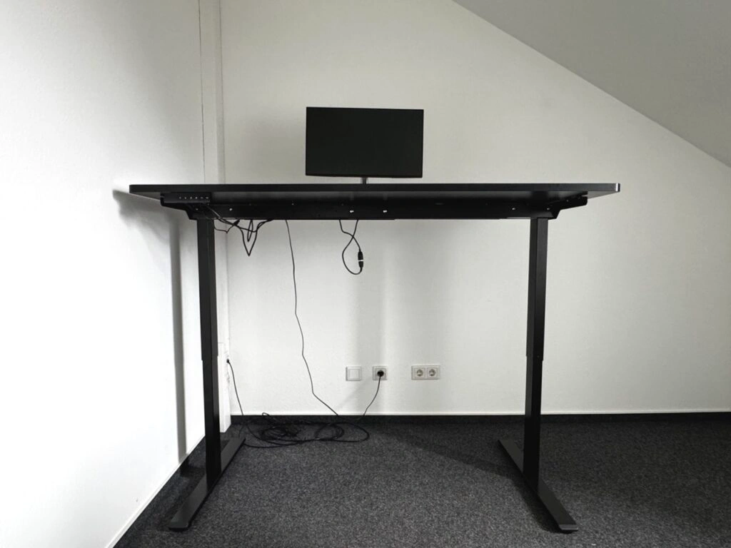 Elektrisch höhenverstellbarer Schreibtisch auf oberster Einstellung, mit Monitor und Tastatur.