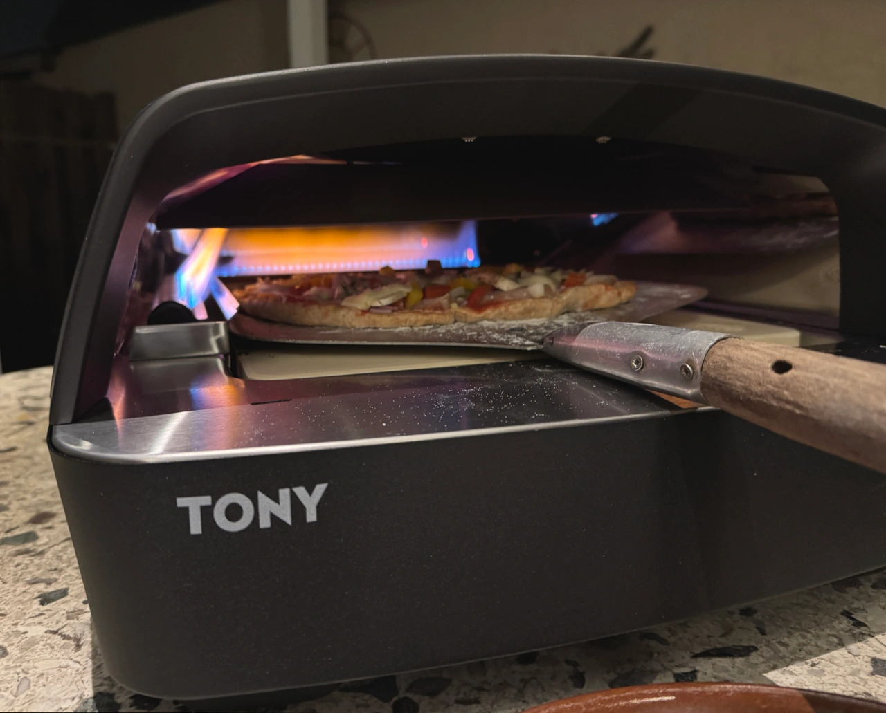Nahansicht des Burnhard Tony, während eine Person Pizzazeit in den Pizzaofen gibt.