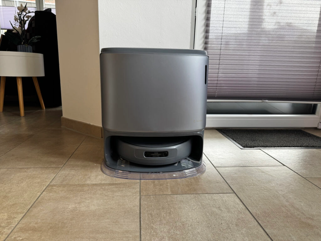 Die Reinigungsstation des Narwal Freo Z10 Ultra steht an einer Wand auf Fliesen. Der Staubsauger-Roboter ist in der unteren Andockposition eingesetzt. Das Gehäuse der Station ist grau und kompakt gestaltet.