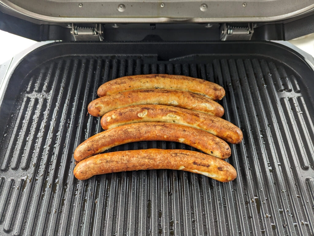Nahaufnahme vier gegrillter Bratwürstchen auf der Grillfläche des Ninja Woodfire Pro XL, die die gleichmäßige Hitzeverteilung verdeutlichen (Foto: Testsieger.de)
