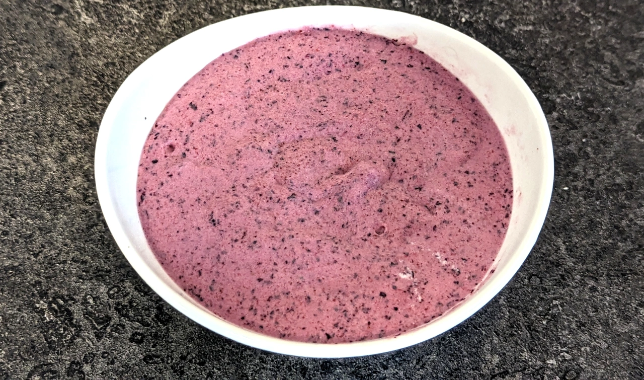 Ansicht von oben auf die pürierten Ergebnisse eines Smoothies aus gefrorenen Erdeeren, Blaubeere und Sahne