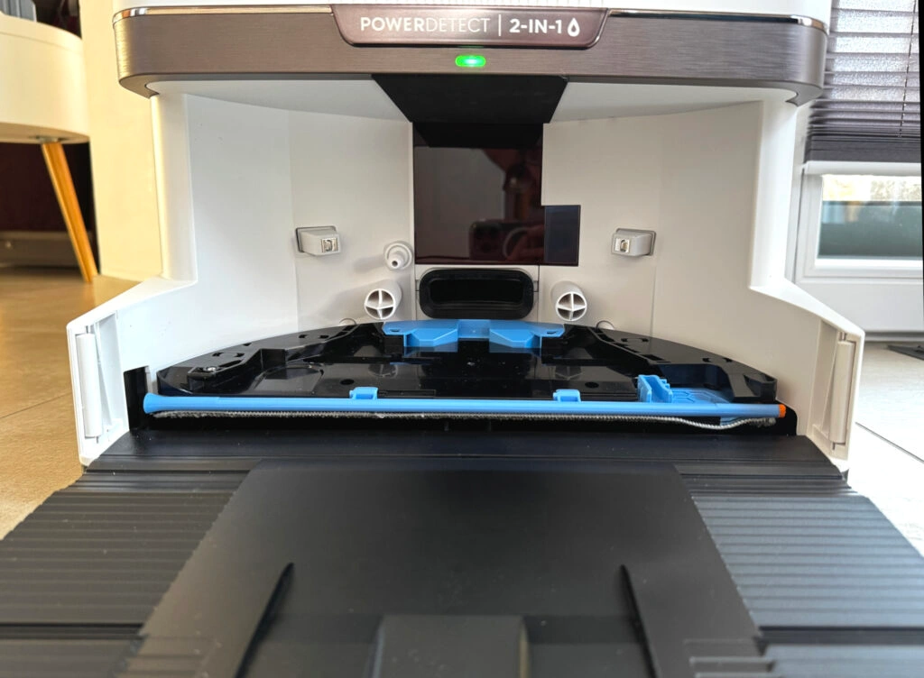 Nahaufnahme des Innenraums der Reinigungsstation des Shark PowerDetect NeverTouch Pro 2-in-1. Die Station verfügt über eine integrierte Selbstreinigungsmechanik mit blauen Halterungen für die Wischpads sowie mehrere Luft- und Wasserdüsen zur Reinigung und Trocknung. Bei Bedarf kann das Wischpad in der Station verbleiben, um Teppiche vor Feuchtigkeit zu schützen.